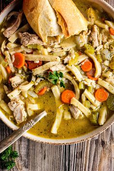 a bowl filled with chicken noodle soup on top of a wooden table next to bread