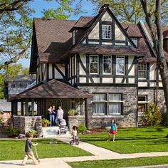 a group of people standing in front of a large house with two kids playing on the lawn