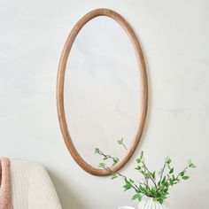 a round mirror hanging on the wall next to a vase with flowers