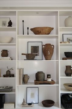 shelves with vases, bowls and other items on them in a white walled room