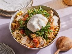 a bowl filled with pasta, meat and vegetables next to two plates on the table