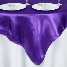 two empty wine glasses sitting on top of a purple table cloth with white plates and silverware