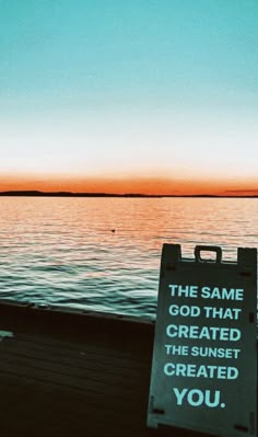 a sign sitting on the side of a body of water with a sunset in the background