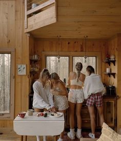 three women are standing in the kitchen preparing food and drinking tea or coffee while another woman looks on