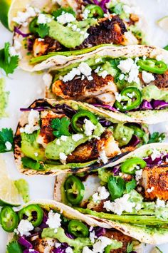 three fish tacos with limes, red cabbage and feta cheese on top