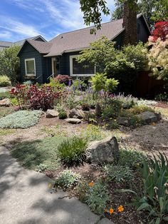 a house with lots of flowers and rocks in the front yard on a sunny day