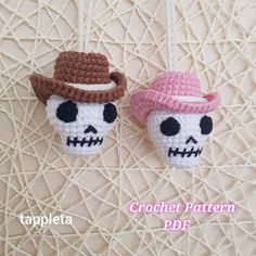 two crocheted skull ornaments hanging from strings with hats on them, one is pink and the other is brown