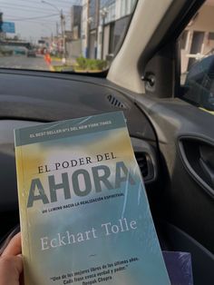 a person is holding up a book in their hand while driving through the city streets