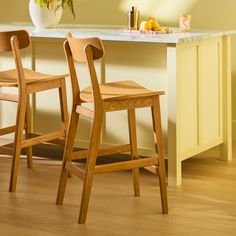 two wooden chairs sitting next to each other in front of a counter with a potted plant on it