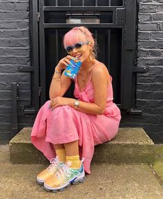 a woman with pink hair and sunglasses sitting on the ground next to a fire place