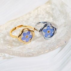 two rings with blue flowers on them sitting on top of a white plate, one is gold and the other is silver