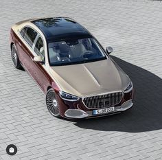 a red and beige car is parked on a brick road next to a building in the city