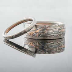 This rustic and unique Mokume Gane ring set features our Woodgrain pattern, an etched & oxidized finish, and a Low Dome profile. This set is made with our "Embers" metal combination that features 14k red gold, Palladium, and sterling silver. ***The price for this set accommodates an 8mm width and a 2mm width. If you would like different widths, please inquire***RING 1Mokume Gane Band Set Width: 8mmPattern: Woodgrain Metal Combo/Palette: Embers Finish: Etched + OxidizedProfile: Low Dome (comf Mokume Gane Ring Wedding, Mokume Gane Ring, Pyrite Ring, Gold Liner, Channel Set Rings, Woodgrain Pattern, Mokume Gane, Custom Wedding Rings, Wedding Band Sets