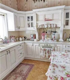 a kitchen with white cabinets and pink flowers on the counter tops, along with a floral table cloth