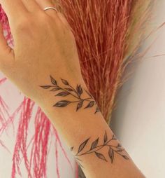 a woman's hand with a tattoo on her left wrist next to red grass