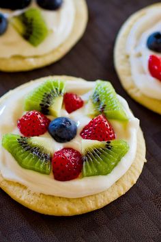 some cookies with fruit and cream on them are sitting on a brown table top, ready to be eaten