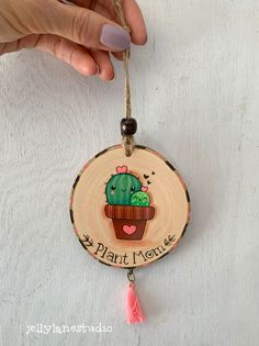 a hand holding a wooden ornament with a cactus on it