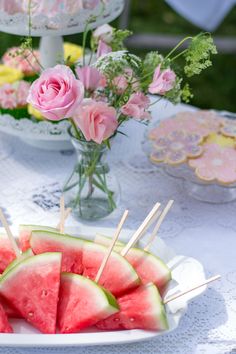 watermelon skewers are arranged on a plate with flowers in the background