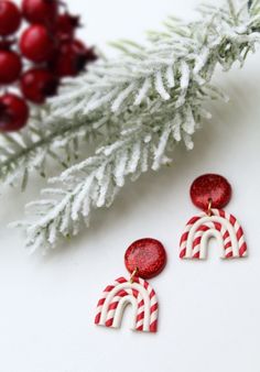 two red and white earrings sitting on top of a table next to a christmas tree