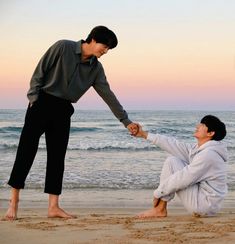 two people on the beach holding hands and touching each other's fingers with one hand