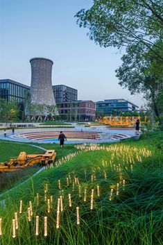 people are walking around in the grass near a pond and power plant with lights on it