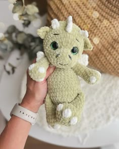 a hand holding a small stuffed animal in front of a white table with flowers on it