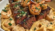 a white bowl filled with pasta and meat covered in sauces, shrimp and garnished with parsley