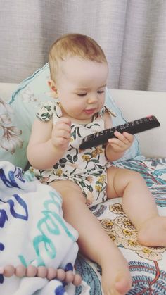 a baby sitting on top of a bed with a remote control in it's hand