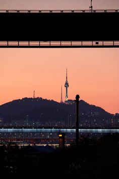 the skyline is lit up at dusk with mountains in the background and a bridge crossing over it