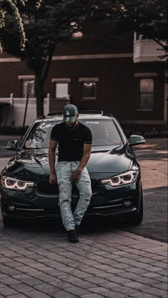 a man sitting on the hood of a black bmw parked in front of a building