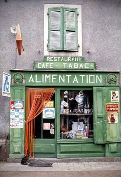 an old green store front on the side of a building with open shutters and windows