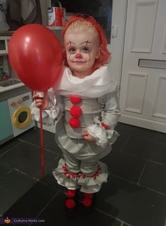 a creepy clown holding a red balloon in the middle of a kitchen with black tile flooring