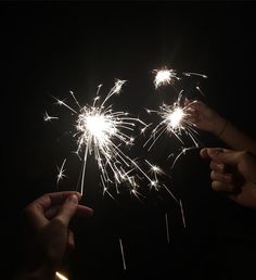 two people holding sparklers in their hands and pointing them at the firecrackers