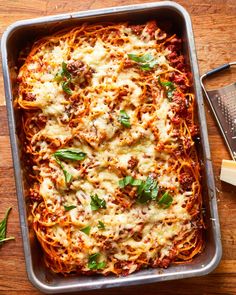 a casserole dish with meat, cheese and sauce on a wooden table next to a grater