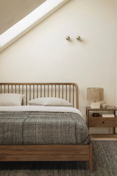 a bed sitting under a slanted ceiling next to a nightstand with a lamp on it