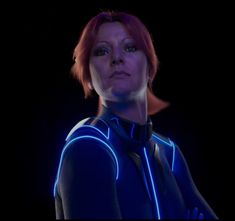 a woman with red hair wearing a blue light up suit and black shirt, standing in the dark