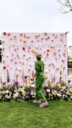 a woman in green jumpsuits walking past a flower display with flowers on it