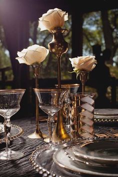 an image of a table setting with white roses in vases and wine glasses on it