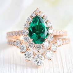 an emerald and diamond ring set on top of a white table