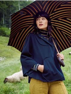 a woman holding an umbrella standing in the grass with sheep behind her on a sunny day