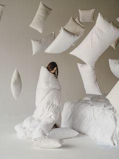 a woman sitting on top of a bed surrounded by pillows and pillows flying in the air