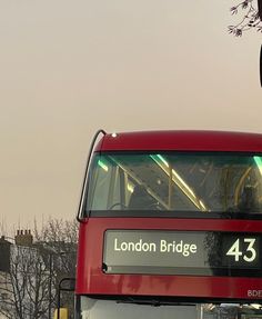 a red double decker bus driving down the street next to a traffic light and trees