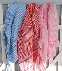 three different colored scarves are hanging on a white wooden fence with blue and pink gingham fabric