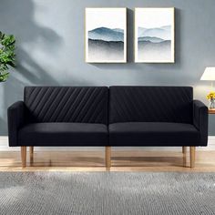 a black couch sitting on top of a wooden floor next to a wall with two paintings above it