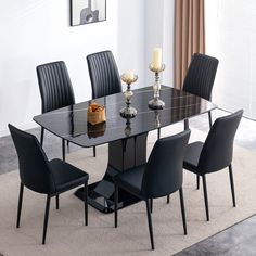 a glass dining table with black chairs and candles on the top, in front of a white wall