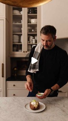 a man standing in a kitchen preparing food on top of a white plate and wearing a scarf