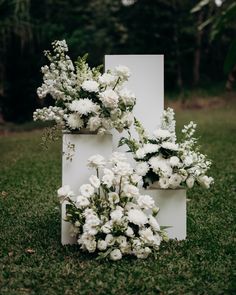 an arrangement of white flowers is placed on top of a tall piece of paper in the grass