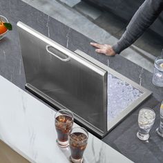 a stainless steel sink in a kitchen with drinks on the counter and someone reaching for it