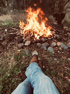 a person sitting in front of a fire with their feet on the ground next to it