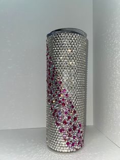 a silver vase with pink and white stones on it's side, against a white wall